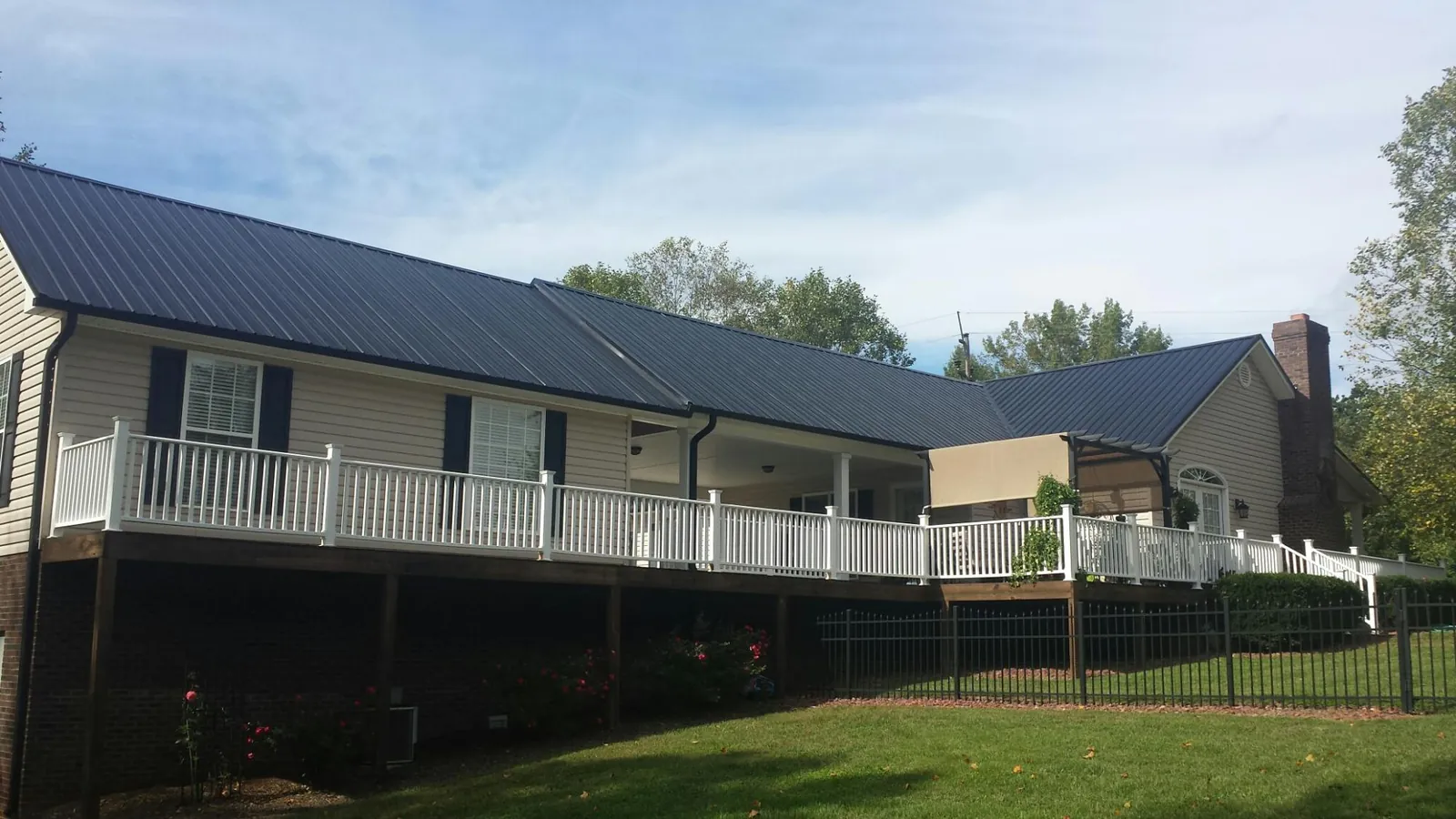 Black metal roof above a long white railed deck on a hillside home in Marshall